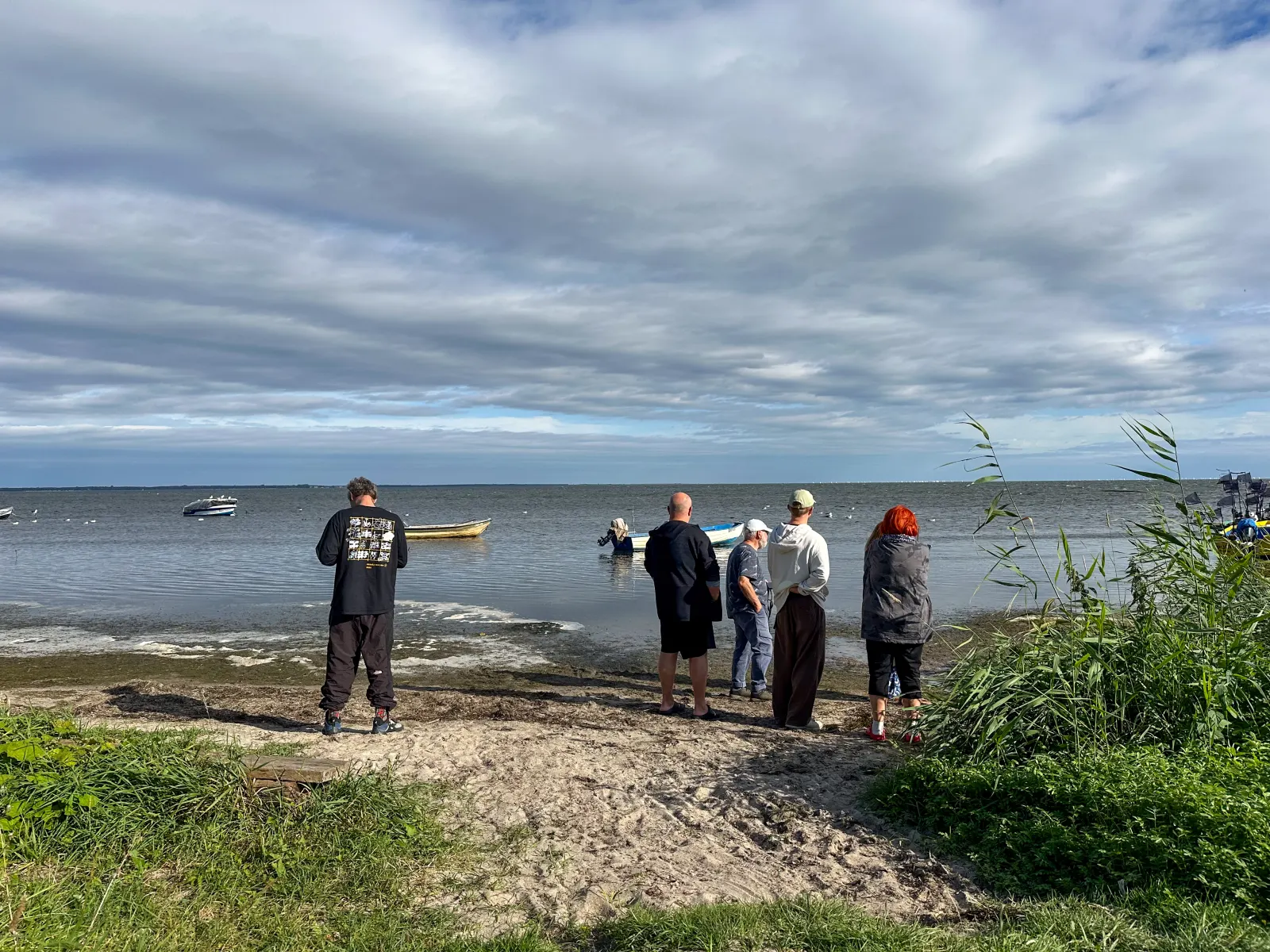 Un grupo de participantes de pie junto a la orilla de la bahía observando los barcos en un día soleado