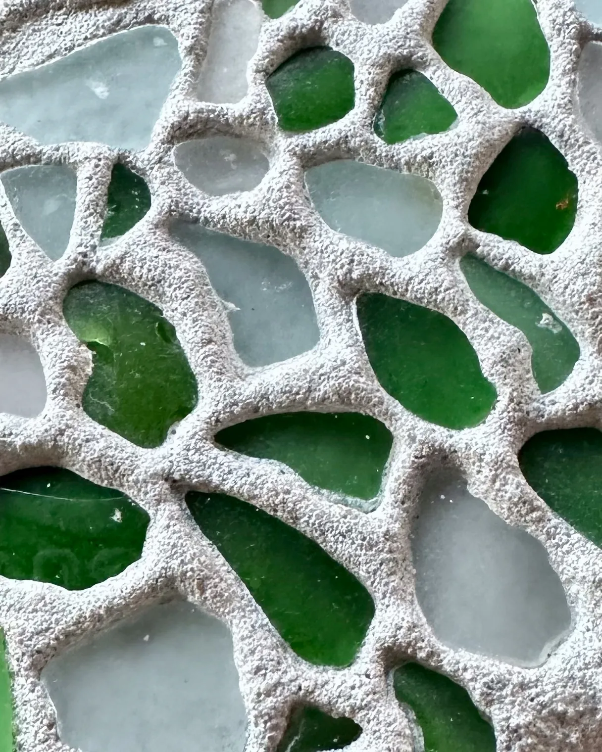 Primer plano de vidrio marino verde y lechoso incrustado en un revoque claro, textura de terrazo