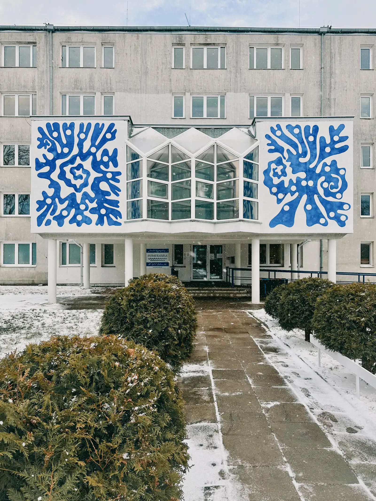 Dos murales azules con forma de coral sobre la fachada blanca de un edificio en invierno